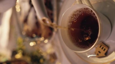 Çaydanlıktan fincana çay dolduran kadın. Noel sofrası. Sıcak çayın yakın çekim görüntüsü, fincandan çıkan buhar. Noel arifesi. Dikey video