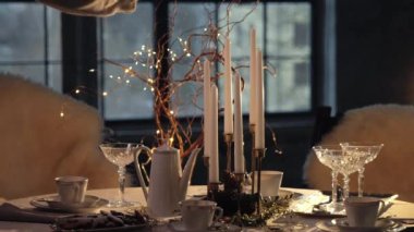 Kadın kibrit kullanarak parafin mumları yakıyor. İçinde fincanlar, çaydanlık, bardaklar ve kurabiyeler olan güzel bir Noel masası. Noel sofrası. Noel arifesine hazırlanıyorum.. 