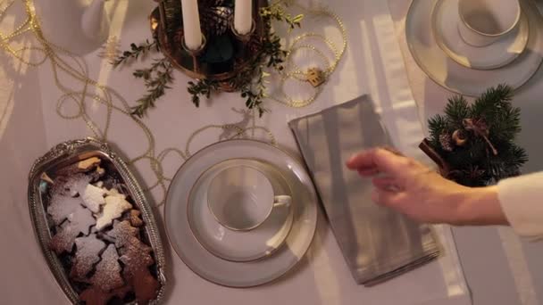 女性の手のクリスマスディナーのテーブルを設定します テーブルには白いテーブルクロス カップ ジンジャーブレッドクッキー テーブルナプキン 小さな木製の装飾家が飾られています — ストック動画