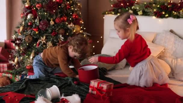 Kisbabák Díszített Hálószobában Játszanak Karácsonykor Gyerekek Berakják Karácsonyi Labdákat Dobozba — Stock videók