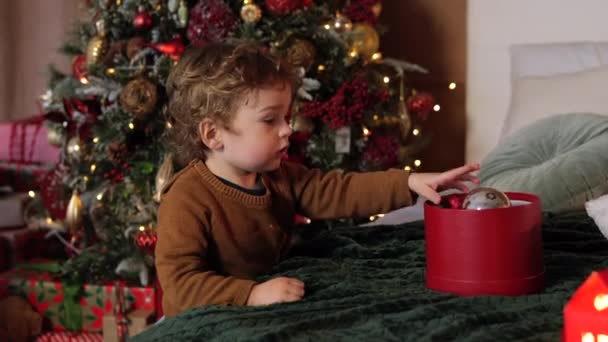 Uroczy Kręcony Chłopczyk Bawiący Się Świątecznymi Kulkami Przytulny Dom Świąteczny — Wideo stockowe