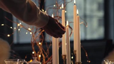 Kadın kibrit kullanarak parafin mumları yakıyor. İçinde fincanlar, çaydanlık, bardaklar ve kurabiyeler olan güzel bir Noel masası. Noel sofrası. Noel arifesine hazırlanıyorum.. 