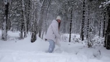 Cameraman playing snowballs with beautiful young woman in warm white woolen jacket, hat and mittens in snowy winter forest