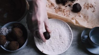 Woman hand in kitchen gloves rolls cream cheese and dark chocolate balls in the plate with coconut flakes 