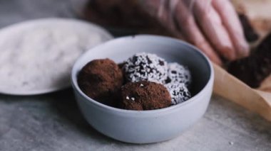Woman hand in kitchen gloves rolls cream cheese and dark chocolate balls in the plate with coconut flakes 