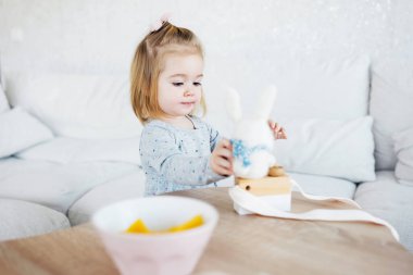 Small adorable girl playing with needle felted rabbit toy in living room