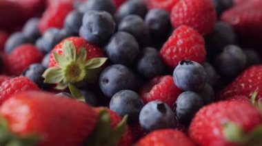 Closeup of fresh tasty blueberries, strawberries and raspberries in rotation. Healthy eating. Summer fruits and berries. Blueberries fall from above