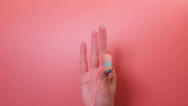 カラフルな爪で女性の手のクローズアップは ピンクの背景に刺激的な手の運動を実行します — ストック動画