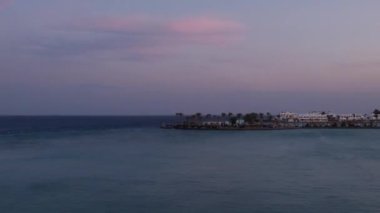 Denizde romantik, renkli bir gün batımı. Palmiye ağaçları ve otel otelleri olan bir yarımada. Gece, şehir ışıklarıyla geceye dönüyor. Zaman ayarlı görüntüler.