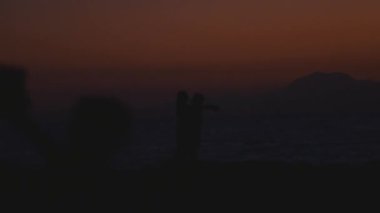 Silhouette of kissing couple against sunset above sea and mountains at public place. Romantic scene of lovers kiss. 