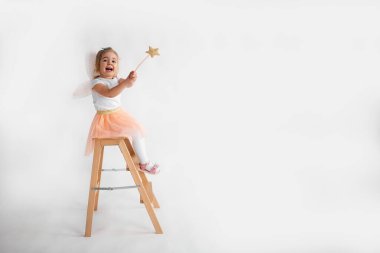 Little fun kid girl princess 2-3 years old wears skirt and fairy wings and holds magic wand fairy stick isolated on white background 