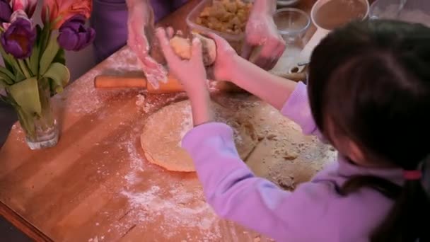 キッチンで一緒にパン屋を準備している幸せな家族 母は台所で圧延ピンで生地をロールアウトします 自家製の食べ物と小さなヘルパー — ストック動画
