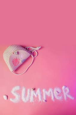 Summer text made of sand and girl straw handbag on pink background with copy space. Summer vacations with children concept