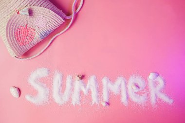 Summer text made of sand and girl straw handbag on pink background with copy space. Summer vacations with children concept