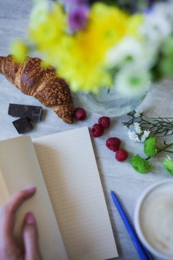 Kadın kahvaltıda arka planda çırpılmış kahve, kruvasan ve sarı kasımpatı ile fotokopi defterini açtı. Sabah ritüelleri