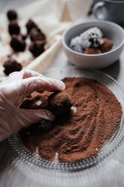 Woman hand in kitchen gloves rolls cream cheese and dark chocolate balls in the plate with cocoa powder