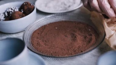 Woman hand in kitchen gloves rolls cream cheese and dark chocolate balls in the plate with cocoa powder