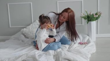 Küçük kızıyla oynayan mutlu genç anne gözlerinin arkasında tatlı çörekler tutuyor. Anne ve kızı birlikte eğleniyorlar.