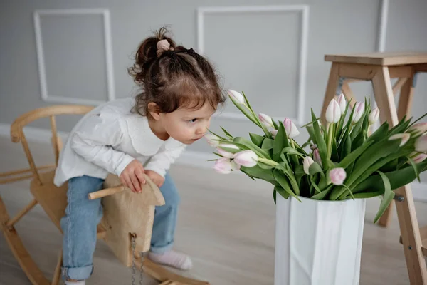 可爱的情绪两岁半的小女孩在一匹木马上荡秋千 在屋里闻郁金香 快乐的童年 — 图库照片