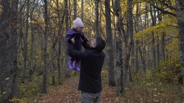 公園で娘と遊ぶ父親は美しい秋の自然を楽しんでいます 幸せな家族の秋の散歩 スローモーション 娘を投げ出して — ストック動画