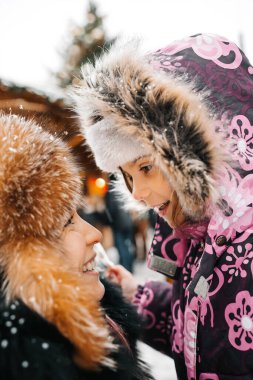 Kız ve anne sıcak giysiler içinde Noel pazarında birbirlerine bakıyorlar. Mutlu tatiller ve mutlu Noeller.