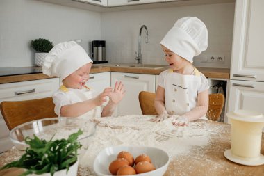 Aşçı şapkalı ve önlüklü sevimli reklamcı kız mutfakta unla oynuyor. Çocuklar hamur hazırlıyor, mutfakta un uçuruyor..