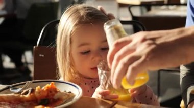 Baba, kızının bardağına kubbe suyu dök. Restoranda portakal suyu içen küçük bir kız. Mutlu aile hafta sonları pizzacıda.
