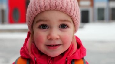 2 yaşındaki pembe şapkalı, kırmızı ceketli, kameraya gülümseyen bir kızın kış portresi.. 