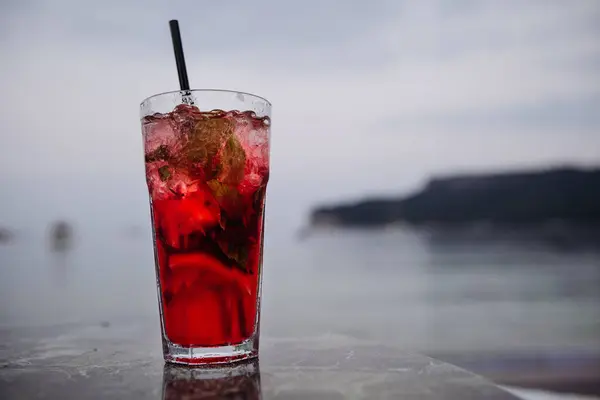 Fresh cold red color alcoholic cocktail on on the table by the sea with mountain view on sunset. Summer sea vacation and travel concept. Copy space