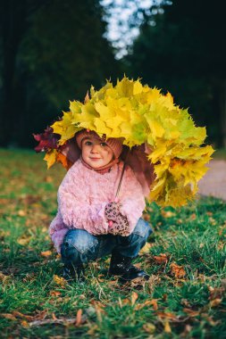 Sarı ve kırmızı akçaağaç yapraklarıyla kaplı küçük bir kızın sonbahar portresi. Altın sonbahar