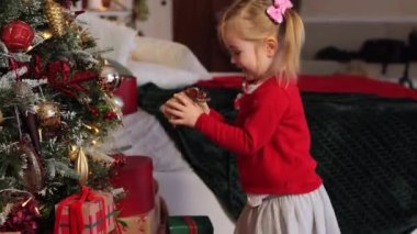 Kırmızı kazaklı iki yaşındaki sevimli kız güzel dekore edilmiş Noel ağacının yanında hediye alıyor. Sıcak Noel evi
