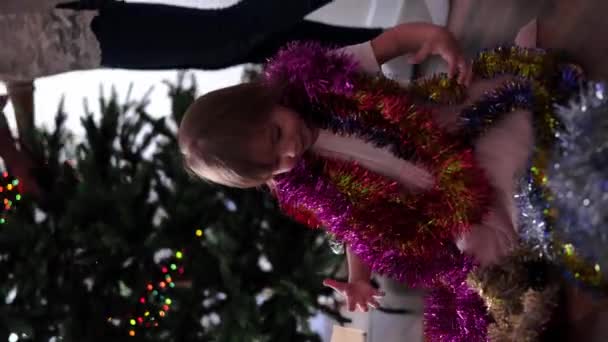 Schattig Klein Meisje Feestelijke Jurk Spelen Met Kerstslingers Gezellig Kersthuis — Stockvideo