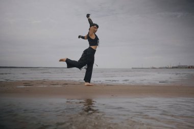 Çağdaş siyah elbiseli dansçı denizde dans ediyor. Modern dans ifadesi, doğayla uyum.