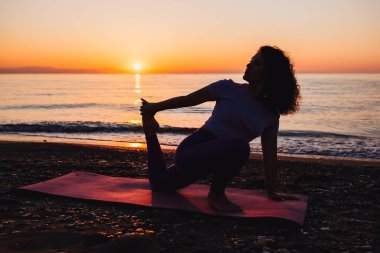Backside view of calm woman yoga practicing by the sea sunrise time. Finding inner peace spiritual healing lifestyle.