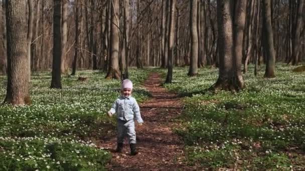 森の中のカメラに向かって走っている小さな3歳の少女は 森の花の花束で白いアネモンで覆われていました ハッピー チャイルド — ストック動画