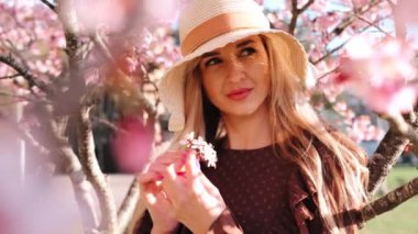 Şapkalı genç, şehvetli sarışın kadının portresi çiçek kokan sakura ağacında duruyor.