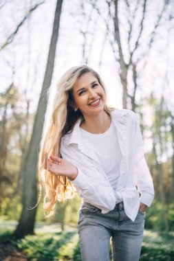 Bahar ormanlarında kameraya bakarak yürüyen uzun saçlı genç bir kadının portresi. Doğanın tadını çıkarıyorum. Eğlence konsepti