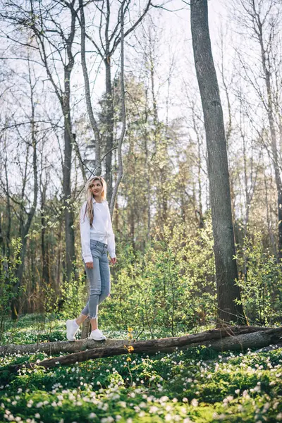 若い女性は 春の森で咲く白い木のエーモンで覆われた森の倒れた木に沿って歩いています 自然を楽しんでいる フリーダムの概念 ストック写真