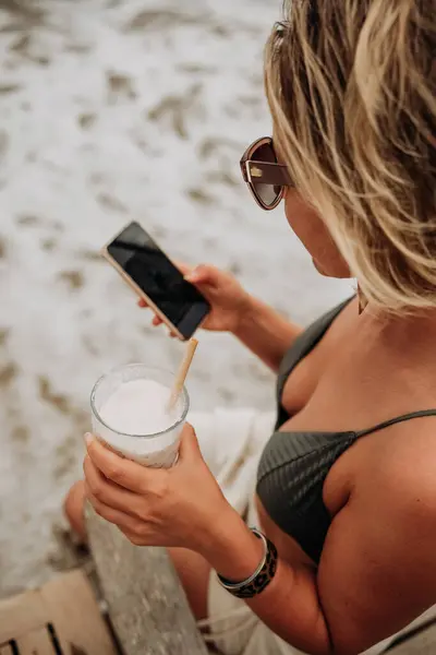 Mujer Joven Bikini Playa Usando Teléfono Móvil Bebiendo Cóctel Fotos de stock