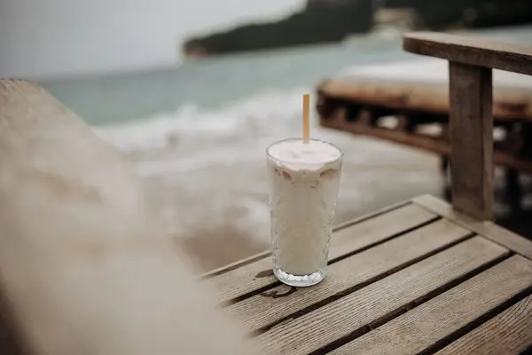 夏休みのコンセプト ヴィンテージカラー ホワイトココナッツアイスクリームカクテル 海による木の椅子 ロイヤリティフリーのストック写真