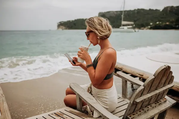 Wanita Muda Dengan Bikini Pantai Menggunakan Ponsel Dan Minum Koktail Stok Gambar Bebas Royalti
