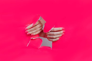 Pembe kağıt delikte manikürlü güzel tırnakları olan kadın elleri.