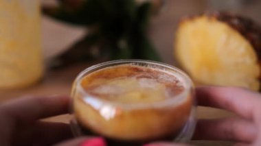 Kadın elleri taze ananas püresi ve espresso kahvesi sunar. Çift tabanlı şeffaf bardakta içecek, bardağın kenarına bir dilim taze ananas koyar..
