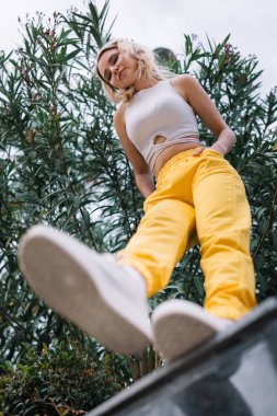 Alçak açılı portre, kaygısız genç kadın, sarı pantolon ve sarı spor ayakkabılar.