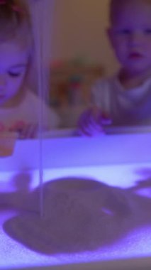 Sevimli 3 yaşındaki çocuk ve kız çocuk odasında duyusal kutuda oynuyorlar. Ellerinde kum süzgeci tutarak