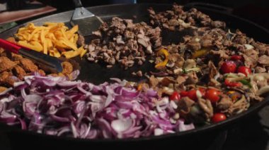 Yakından bakınca, şef et, kızarmış patates, falafel ve sebzeleri kızartma tavasında pişiriyor.