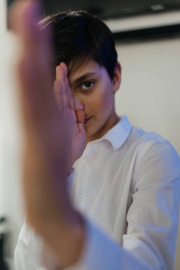 Yüzünün yarısını elinin arkasına saklayan sevimli bir gencin portresi. Kameraya bakıyorum.