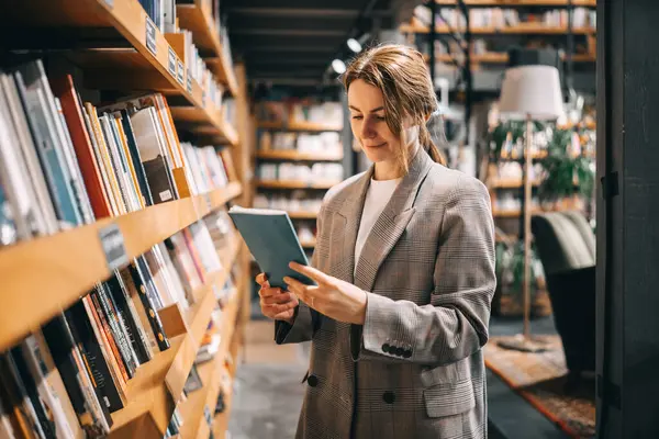Kitapçıda ya da kütüphanede kitaptan alınmış kitaplara bakan genç bir kadın..