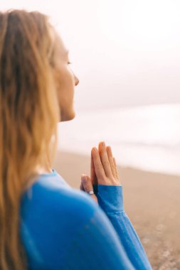 Spor elbiseli genç kadın deniz kenarında meditasyon yapıyor, sabahları plajda sakinleştirici ve topraklama egzersizleri yapıyor.. 
