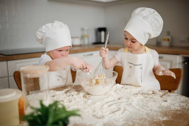 Un mutfak masasını kaplarken, iki genç çocuk bir kasede malzemeleri karıştırarak enfes bir yemek pişirme aktivitesine girişiyor..